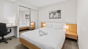 Ein Hotelzimmer mit Bett, Schreibtisch, Stuhl, Nachttisch mit Lampe und Spiegel.