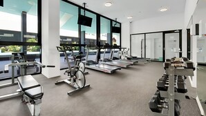 Ein modernes Fitnessstudio mit Cardiogeräten, Gewichtsbänken und großen Fenstern mit Blick ins Freie.