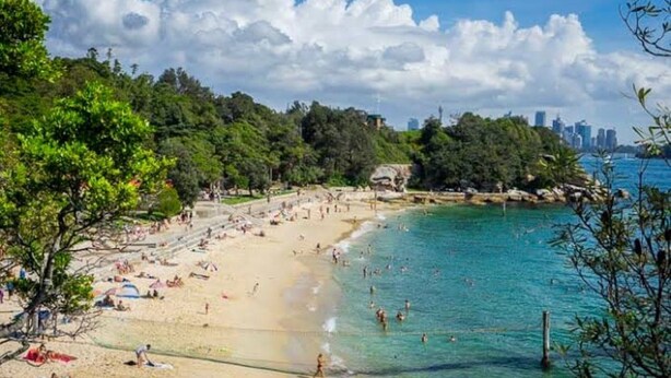 A beach with clear turquoise water, people sunbathing, and a city skyline in the background. - Bright 2-bed Flat With Balcony in Vaucluse (Sydney)