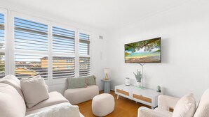 A modern living room with a large window, a flat-screen TV, and a minimalist decor. - Bright 2-bed Flat With Balcony in Vaucluse (Sydney)