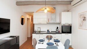 A modern kitchen with white cabinets, a dining table set for four, and a TV on the left.