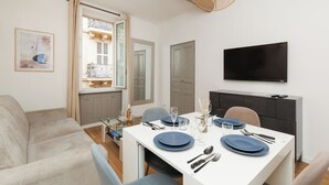 A dining area with a white table set for four, a television above, and a window with curtains.