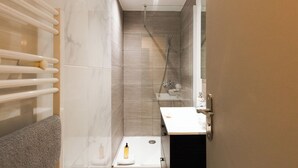 A modern bathroom with a glass shower enclosure, a white sink, and a towel rack.