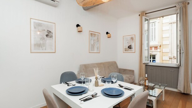 A dining area with a white table set for four, a sofa, and a window with curtains.