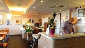 A reception area with a counter, chairs, and a man standing. - ibis budget Montauban Les Chaumes (Montauban)