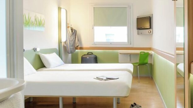 A hotel room with two beds, a desk, a chair, a television, and a window. - ibis budget Montauban Les Chaumes (Montauban)