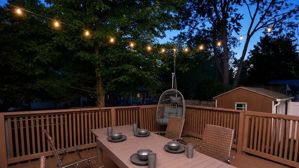 Una terraza al aire libre con una mesa, sillas, luces colgantes y una silla colgante.