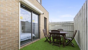 En lille terrasse med et bord og stole, en skydedør samt et træhegn.