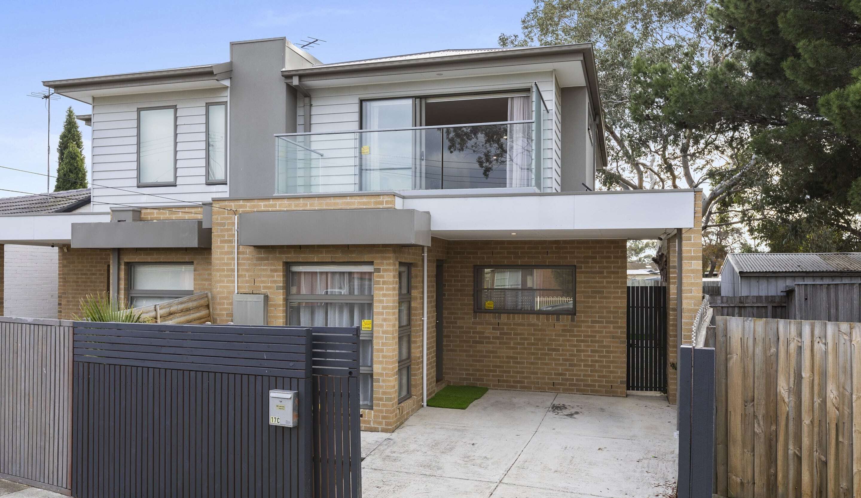 A two-story residential building with a balcony, a garage, and a fenced yard.
