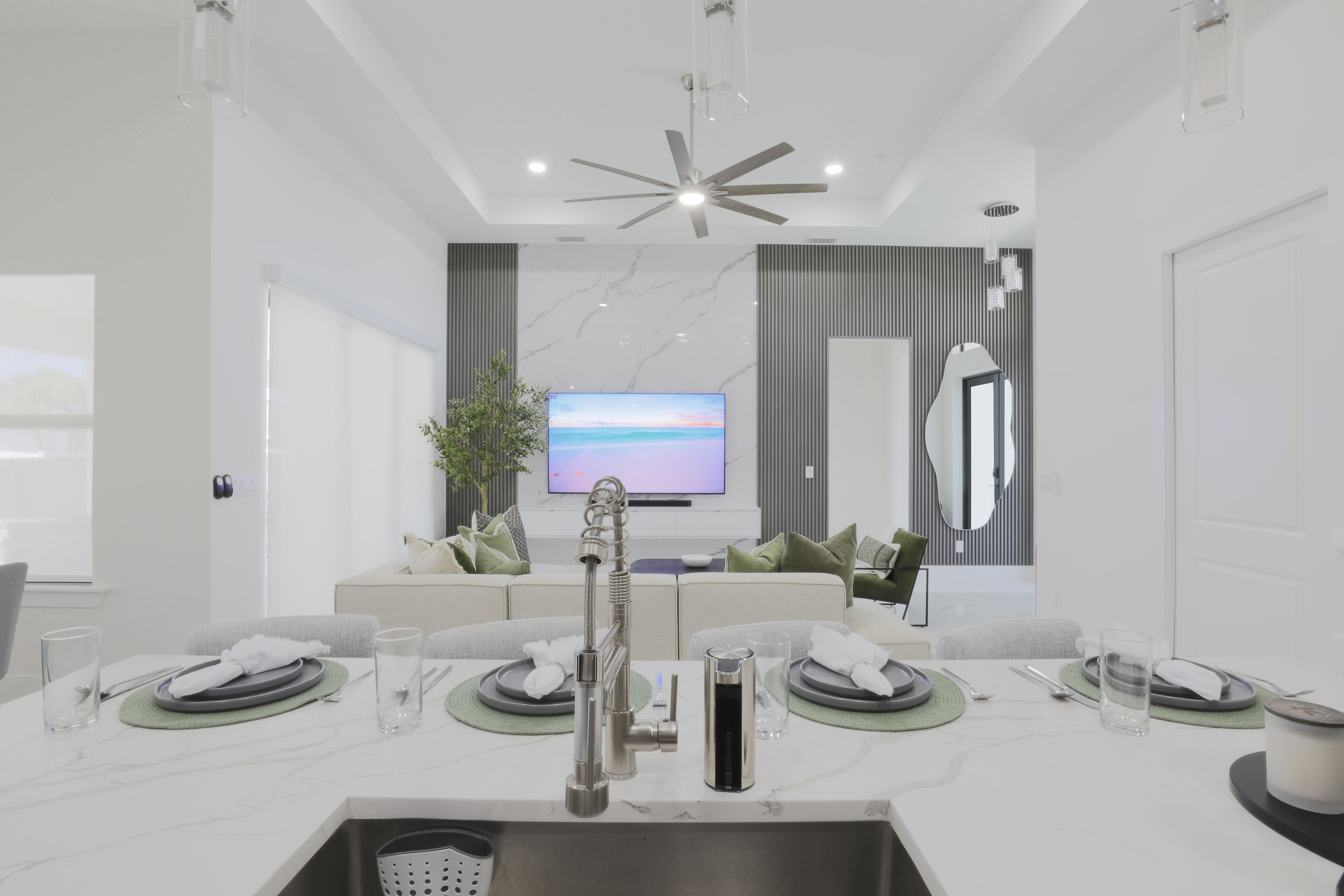 Une cuisine moderne dotée d’un évier encastré, d’un ventilateur de plafond et d’un grand téléviseur à écran plat fixé au mur.