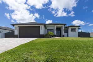 A modern two-story house with a garage, a well-maintained lawn, and a clear blue sky. - Is This Cape`s Best Secret? | 4BR Midnight Pool (Cape Coral)