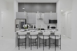 A modern kitchen with a central island, bar stools, and a built-in microwave. - Is This Cape`s Best Secret? | 4BR Midnight Pool (Cape Coral)