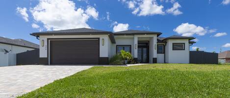 A modern two-story house with a garage, a well-maintained lawn, and a clear blue sky.