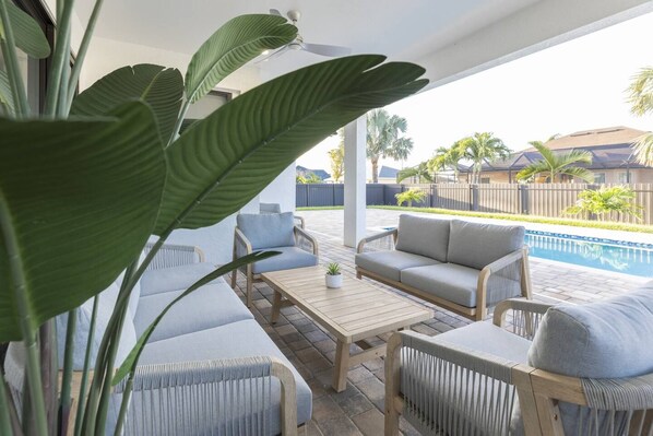 An outdoor patio area with a pool, seating, and large green plants.