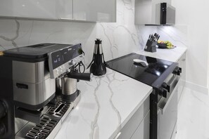 A modern kitchen with a coffee machine, a stove, and a countertop with a knife block and fruit.