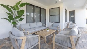A modern outdoor seating area with a grey sofa, wicker chairs, and a wooden coffee table.