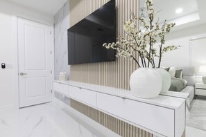 Una sala moderna con un televisor de pantalla plana montado en la pared, una consola blanca con un florero y un sofá con cojines.