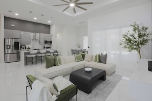 A modern living room with a sofa, coffee table, and a dining area with chairs. - Is This Cape`s Best Secret? | 4BR Midnight Pool (Cape Coral)