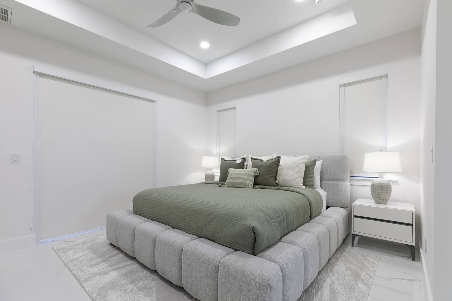 Une chambre moderne avec un grand lit, des tables de chevet, un ventilateur de plafond et un grand miroir.
