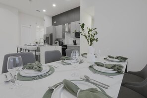 Een moderne eethoek met een witte tafel gedekt voor een maaltijd, grijze stoelen en een keuken op de achtergrond.