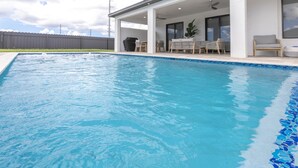 A swimming pool with a covered patio area, outdoor furniture, and a view of the sky.