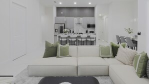 A modern living room with a sofa and a dining area in the background.
