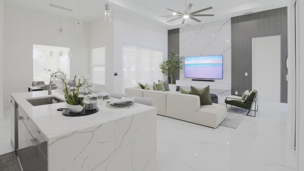 A modern kitchen with a marble island, a dining area with a sofa, and a TV in the living room.