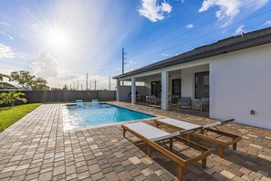 A swimming pool with lounge chairs, a covered patio area, and a brick patio.
