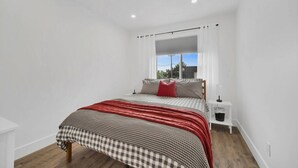 Ein Schlafzimmer mit einem Bett, einem Nachttisch, einem Fenster mit Vorhängen und Blick ins Freie.