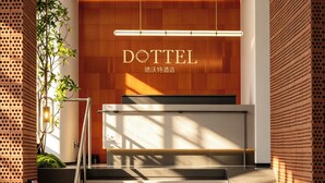 A modern hotel reception area with a wooden reception desk, a staircase, and a security camera. - DOTTEL HOTEL (Shantou)