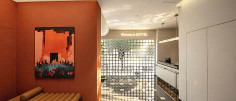 Un moderno vestíbulo de hotel con un mostrador de recepción, un banco, una pared con un cuadro de un paisaje urbano y un cartel de bienvenida.