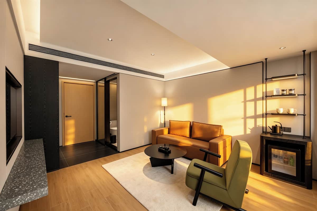 A modern living room with a sofa, coffee table, and armchair, a fireplace, and a built-in shelf with items.