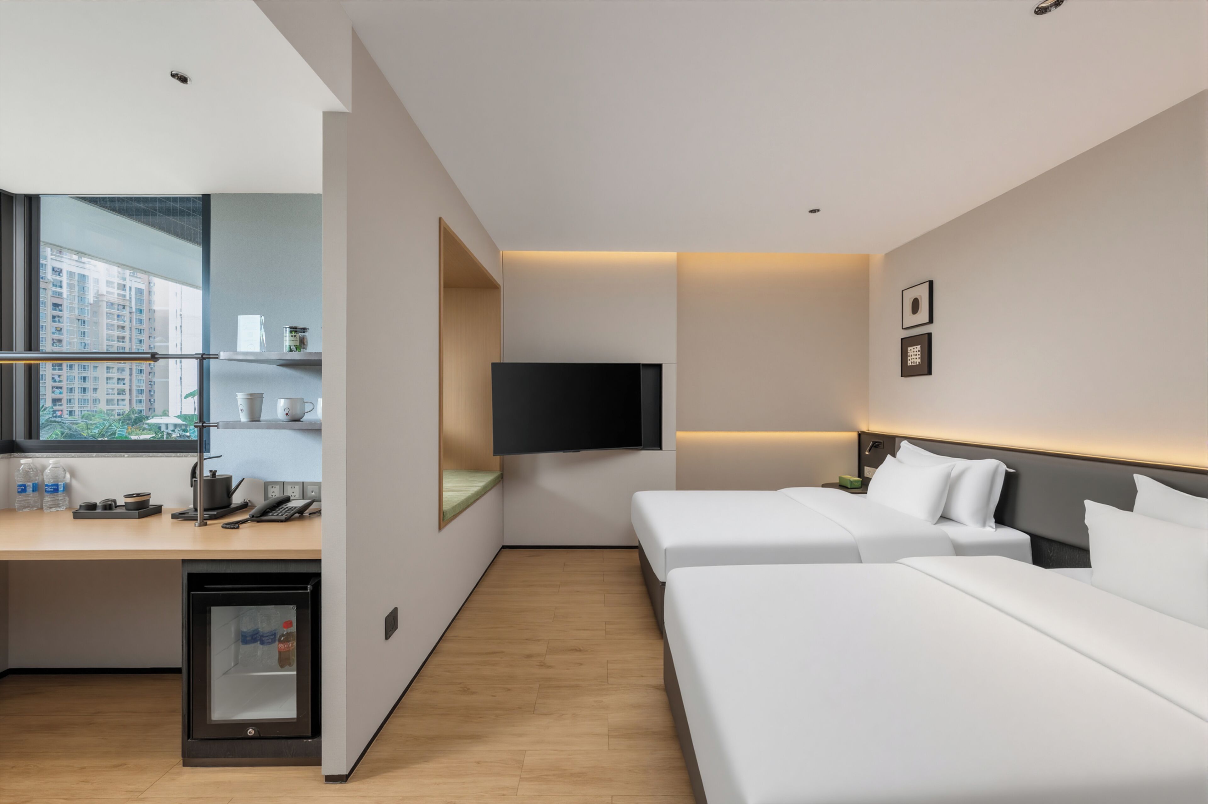 Una habitación de hotel con escritorio, dos camas, televisor y refrigerador pequeño.