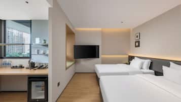 Una habitación de hotel con escritorio, dos camas, televisor y refrigerador pequeño.