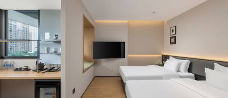 Una habitación de hotel con escritorio, dos camas, televisor y refrigerador pequeño.