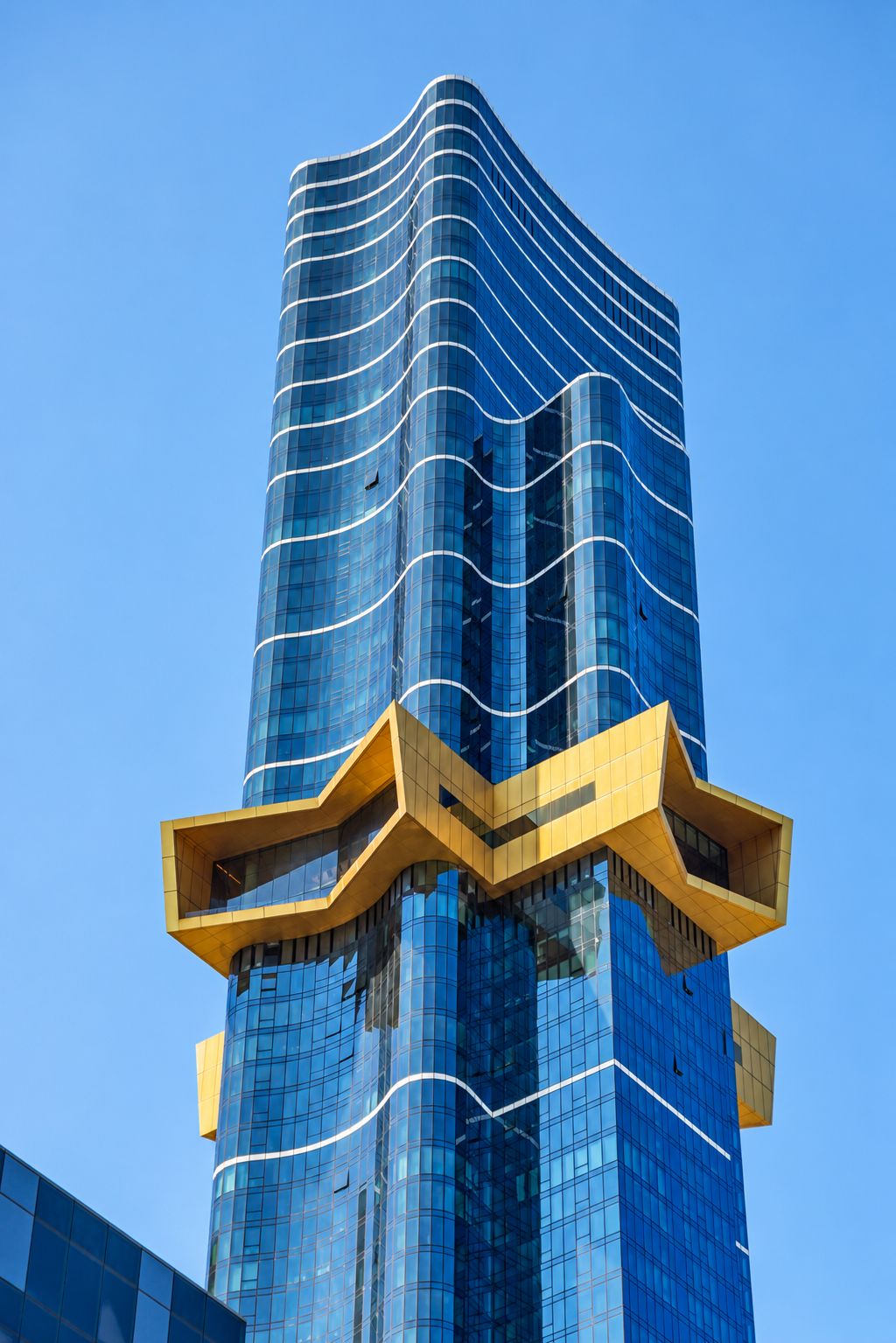 A tall, modern building with a curved glass facade and a distinctive yellow structural element at the base.