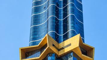 A tall, modern building with a curved glass facade and a distinctive yellow structural element at the base.