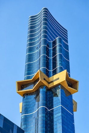 A tall, modern building with a curved glass facade and a distinctive yellow structural element at the base.