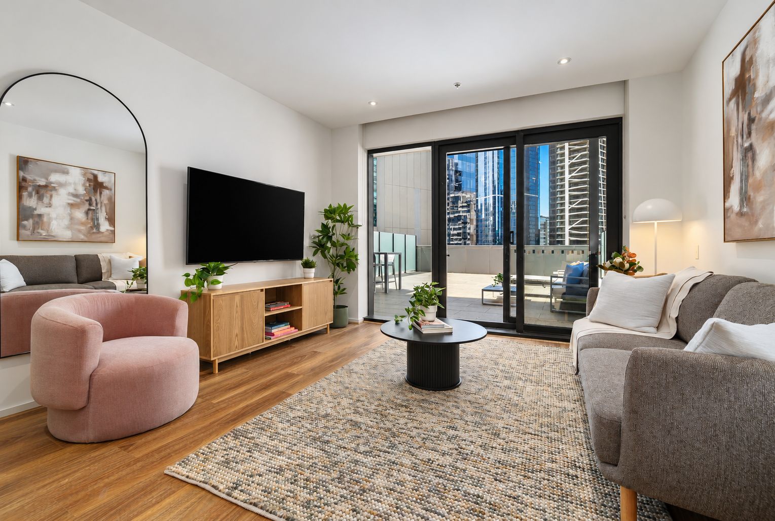 A modern living room with a flat-screen TV, a pink armchair, a grey sofa, and a wooden entertainment unit.