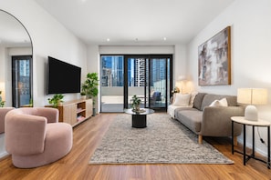 A modern living room with a flat-screen TV, a sofa, a coffee table, and a large window with a city view.