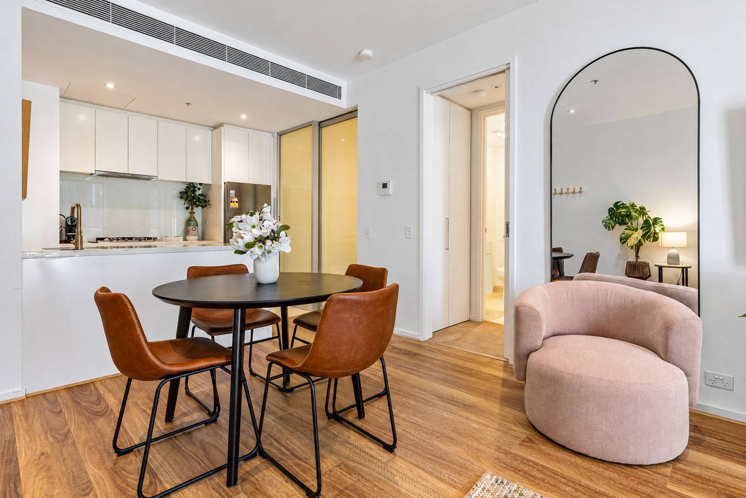 A modern kitchen with white cabinets, a dining table with chairs, and a large mirror.