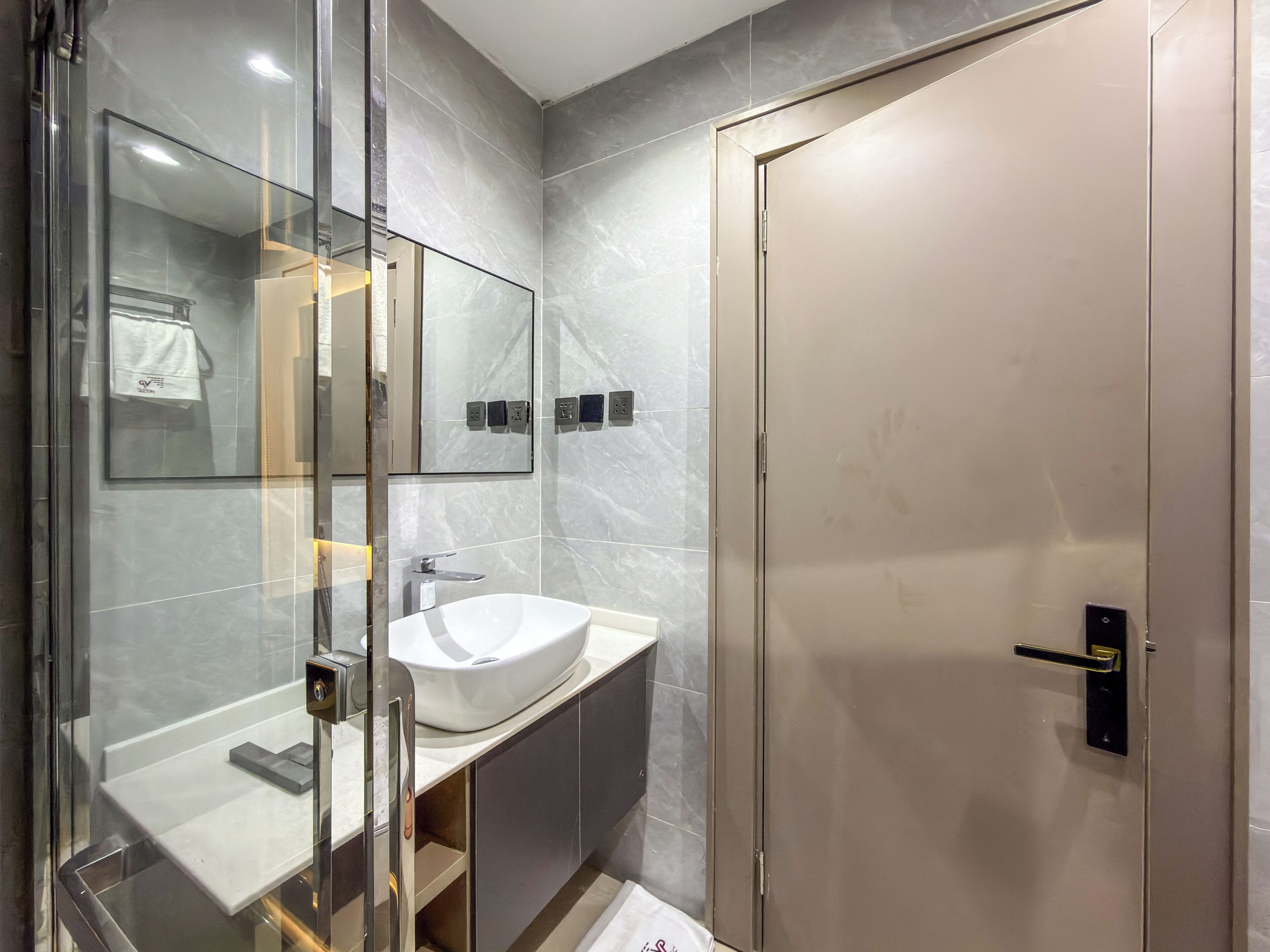 A modern bathroom with a glass shower enclosure, a white sink, and a door with a handle.