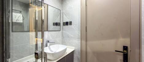 A modern bathroom with a glass shower enclosure, a white sink, and a door with a handle.