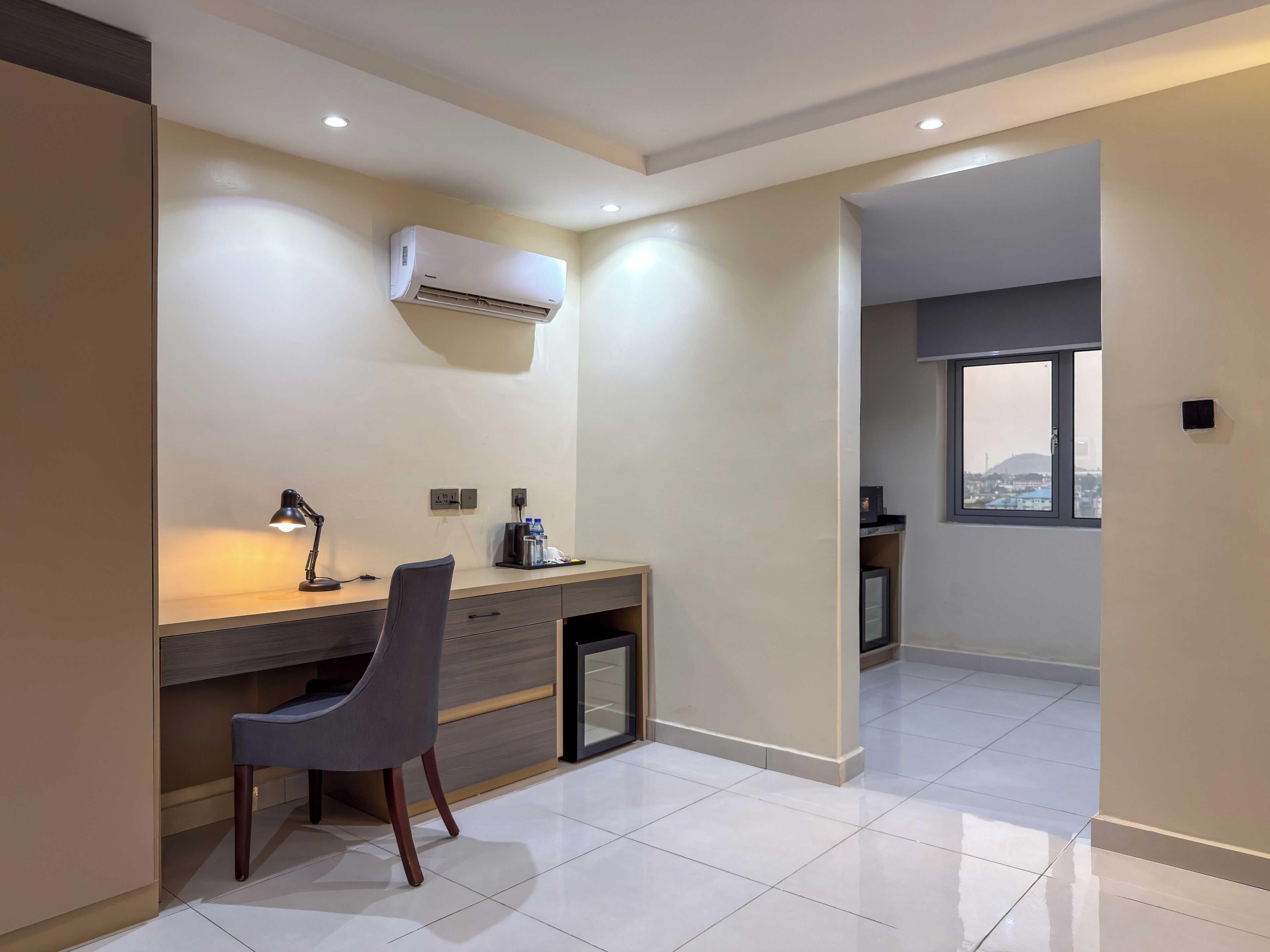 Un espacio de oficina moderno con escritorio, silla, equipo de aire acondicionado y vistas por una ventana.