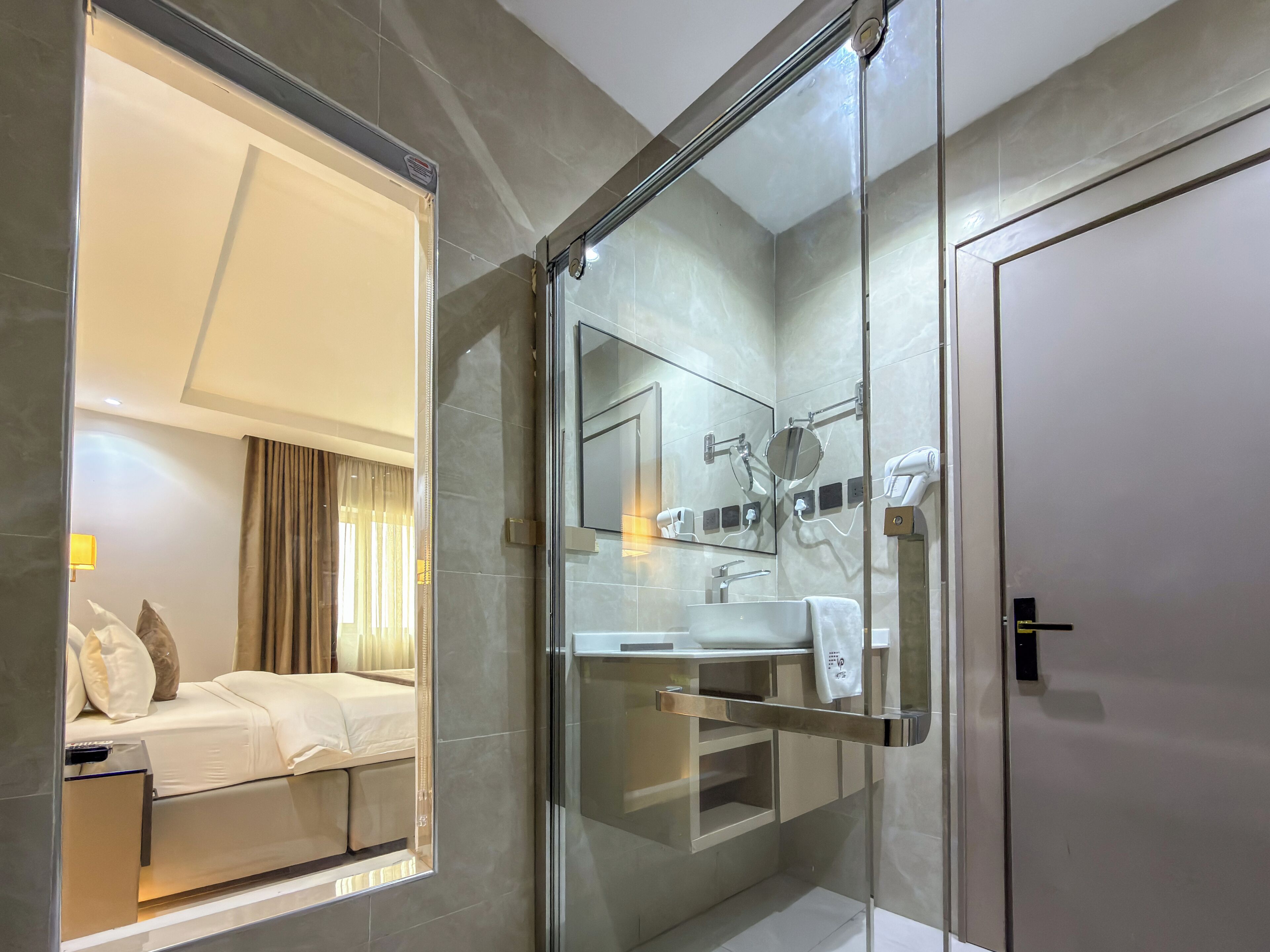 Een moderne badkamer met een douchecabine van glas, een grote spiegel en een wastafel met handdoekhouder.
