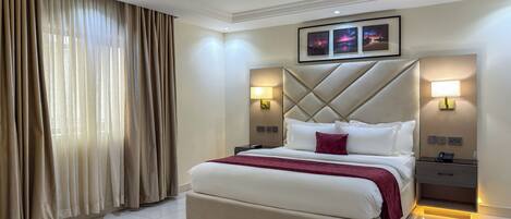 Una habitación de hotel con una cama grande, dos mesitas de noche, un cabecero con diseño de rombos y una ventana con cortinas.