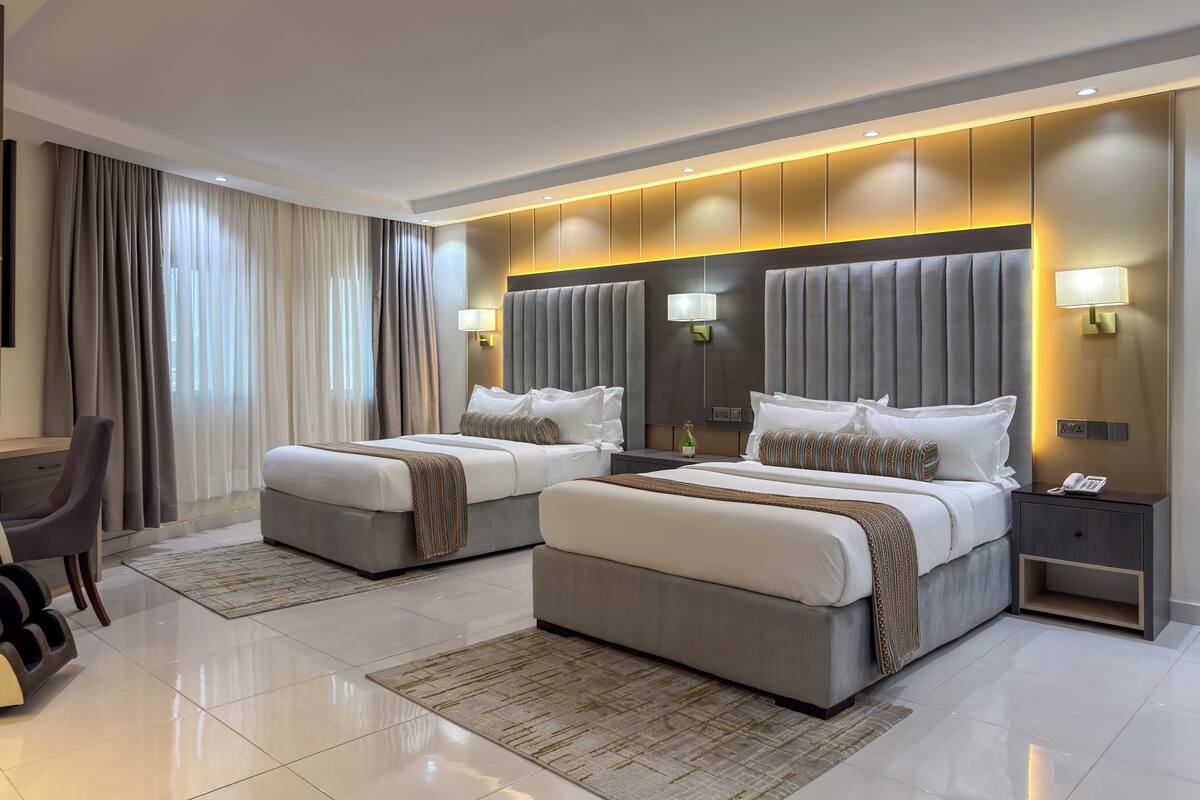A modern hotel room with two beds, a desk, and a chair.