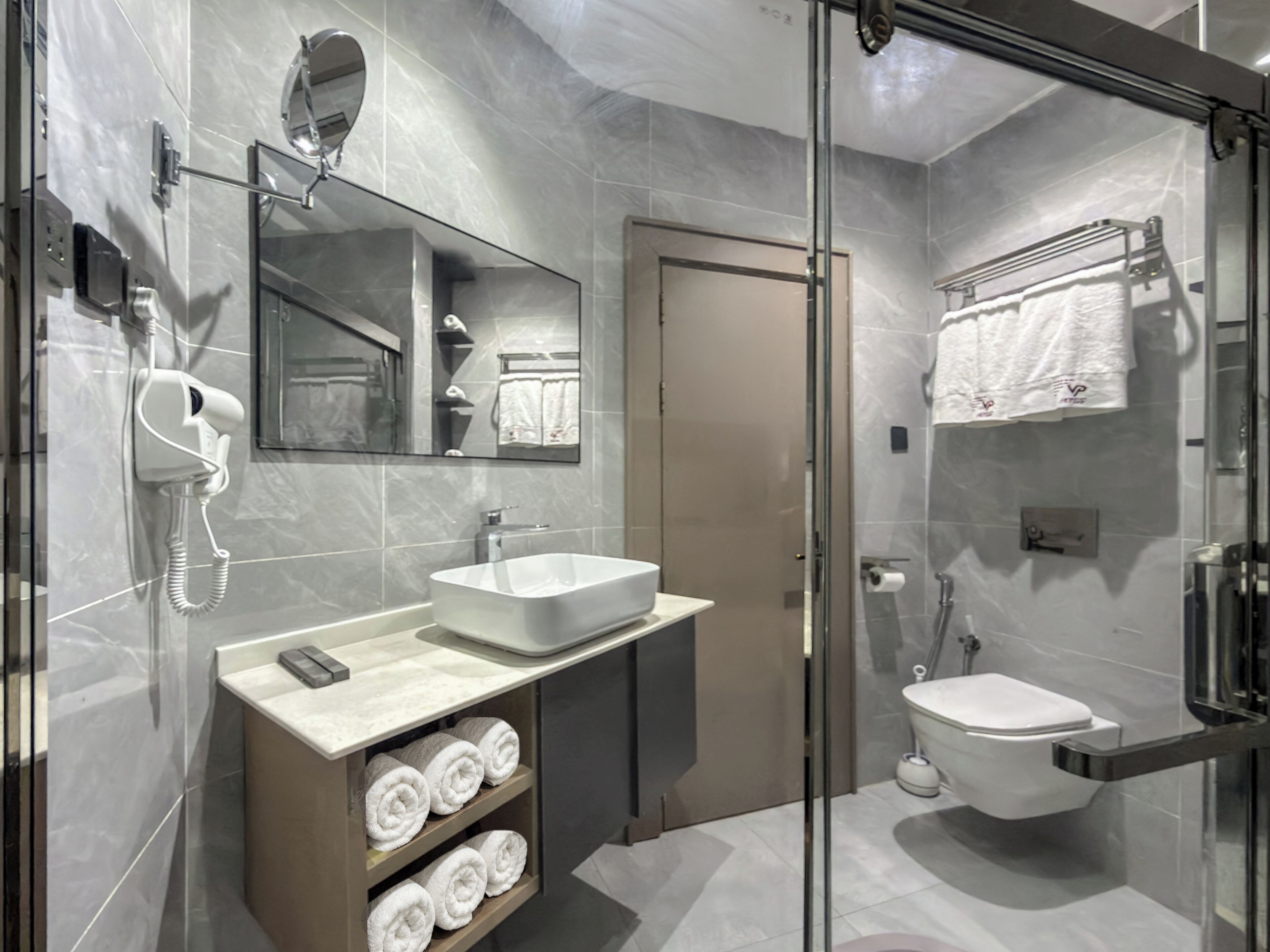 A modern bathroom with a glass-enclosed shower, a sink with a towel rack, and a toilet.