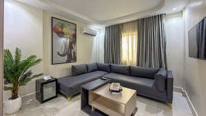 A modern living room with a sectional sofa, a small coffee table, a potted plant, a side table, and a wall-mounted TV.