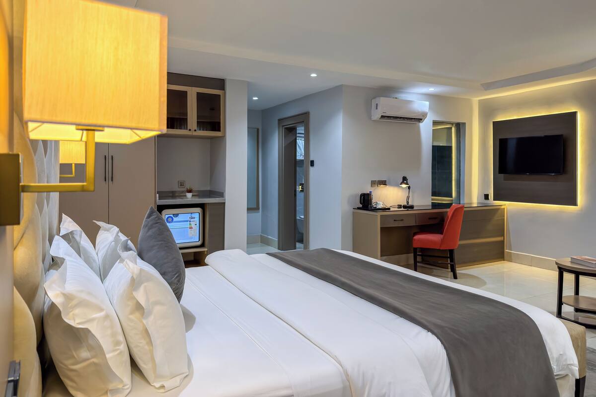 A modern hotel room with a bed, desk, chair, TV, and a computer.